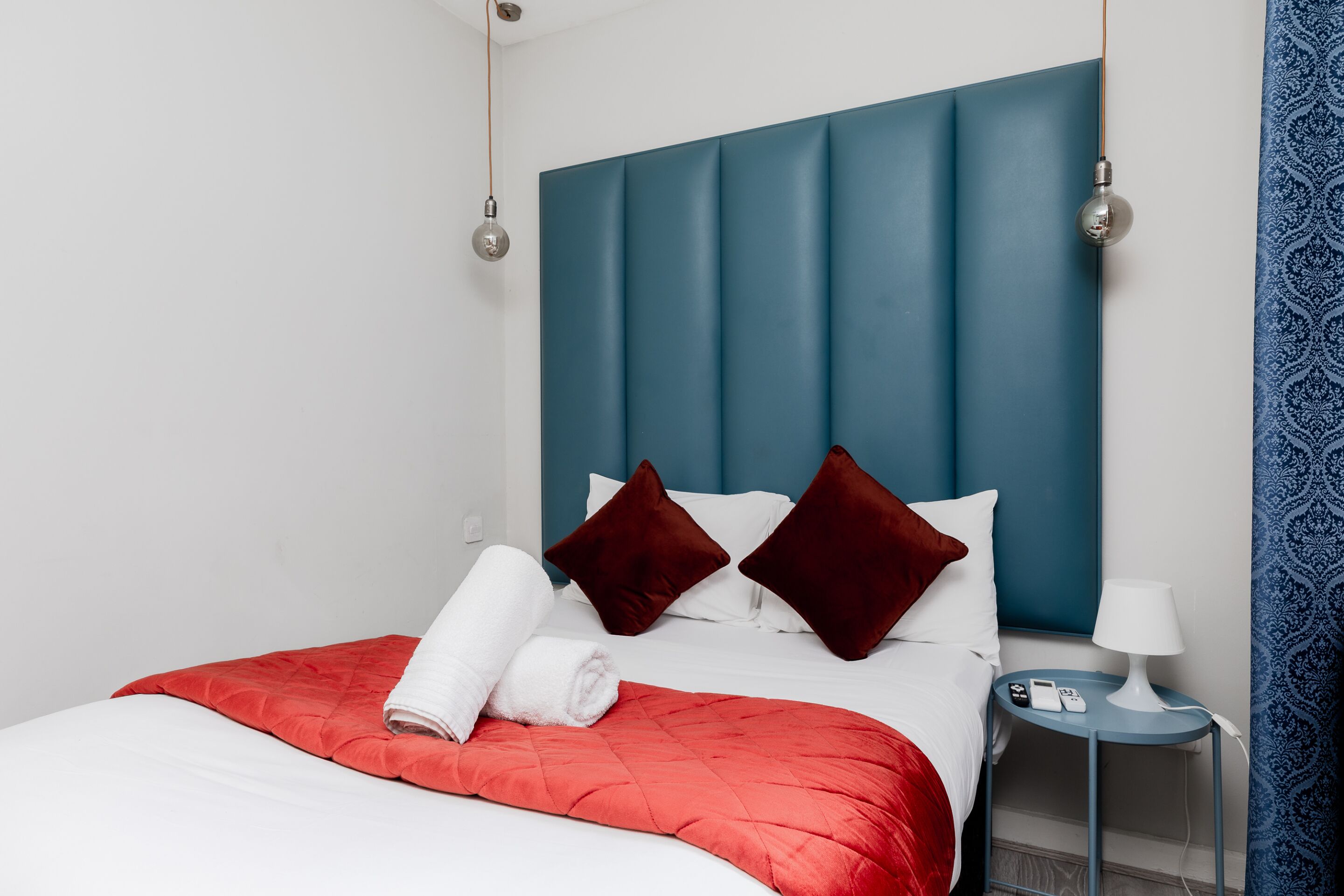 A hotel room with a bed, a nightstand, a lamp, and a blue headboard.