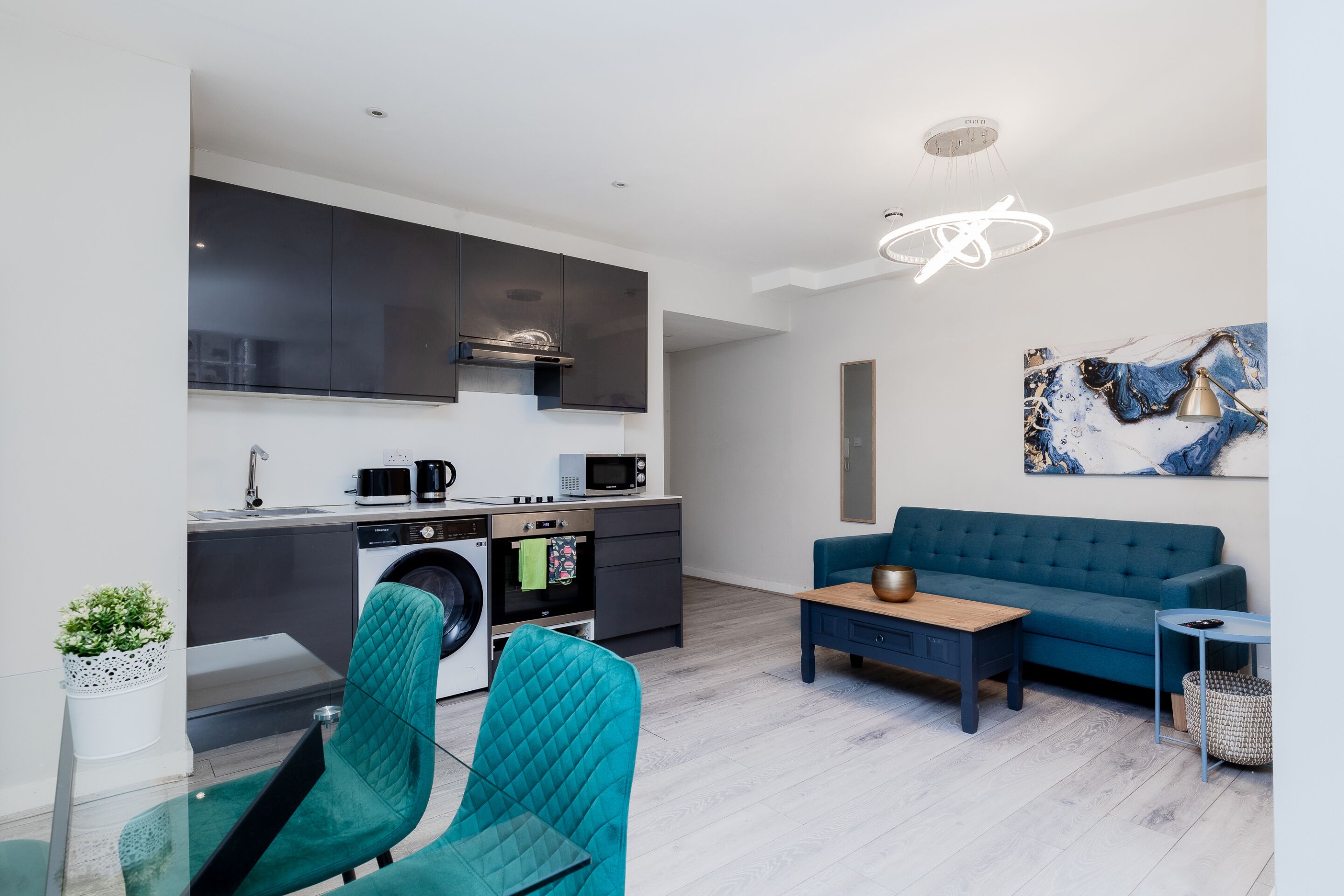 A modern living space with a kitchen, a blue sofa, and a dining area.