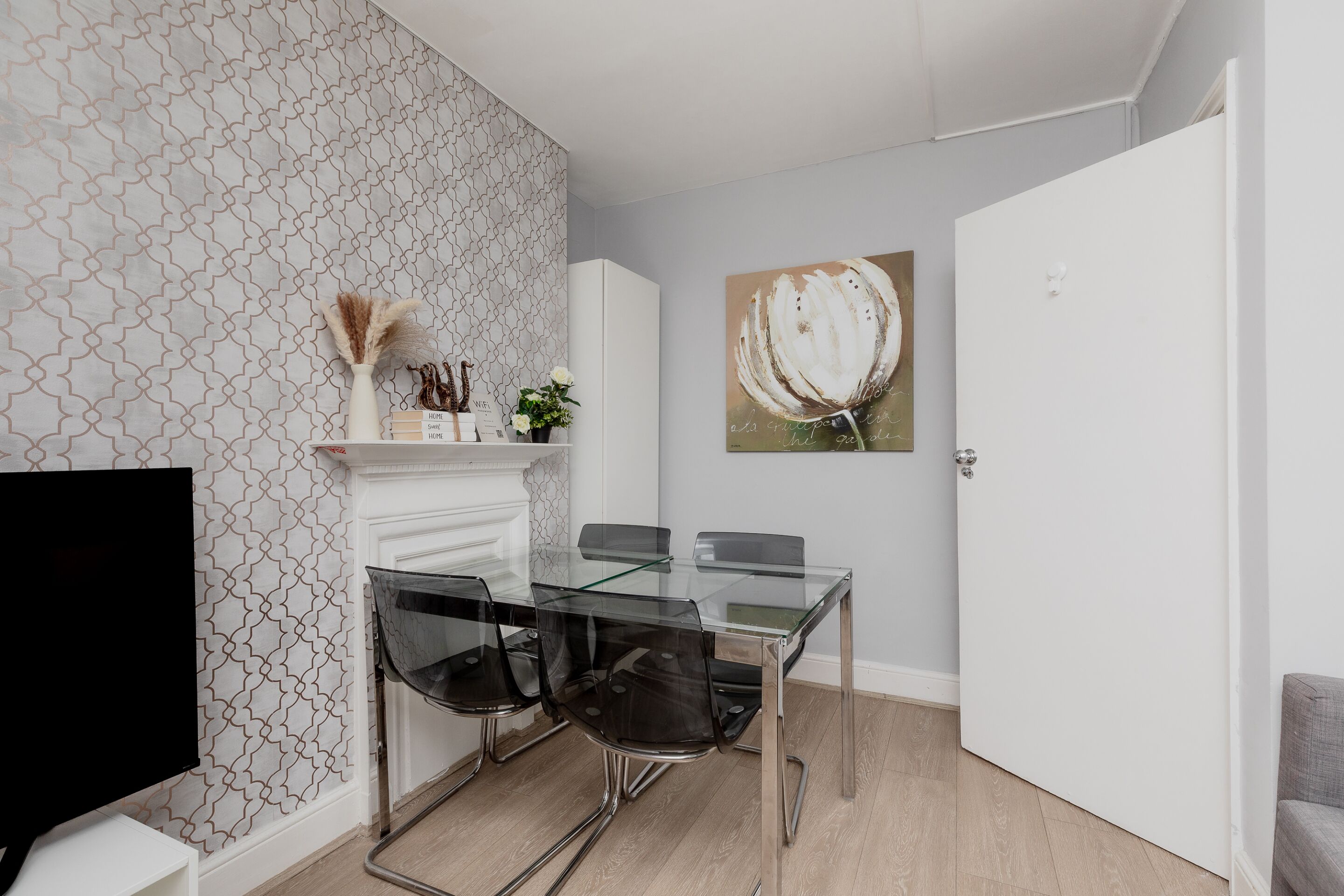 A modern dining area with a glass table, four chairs, a TV, a fireplace, and a painting on the wall.