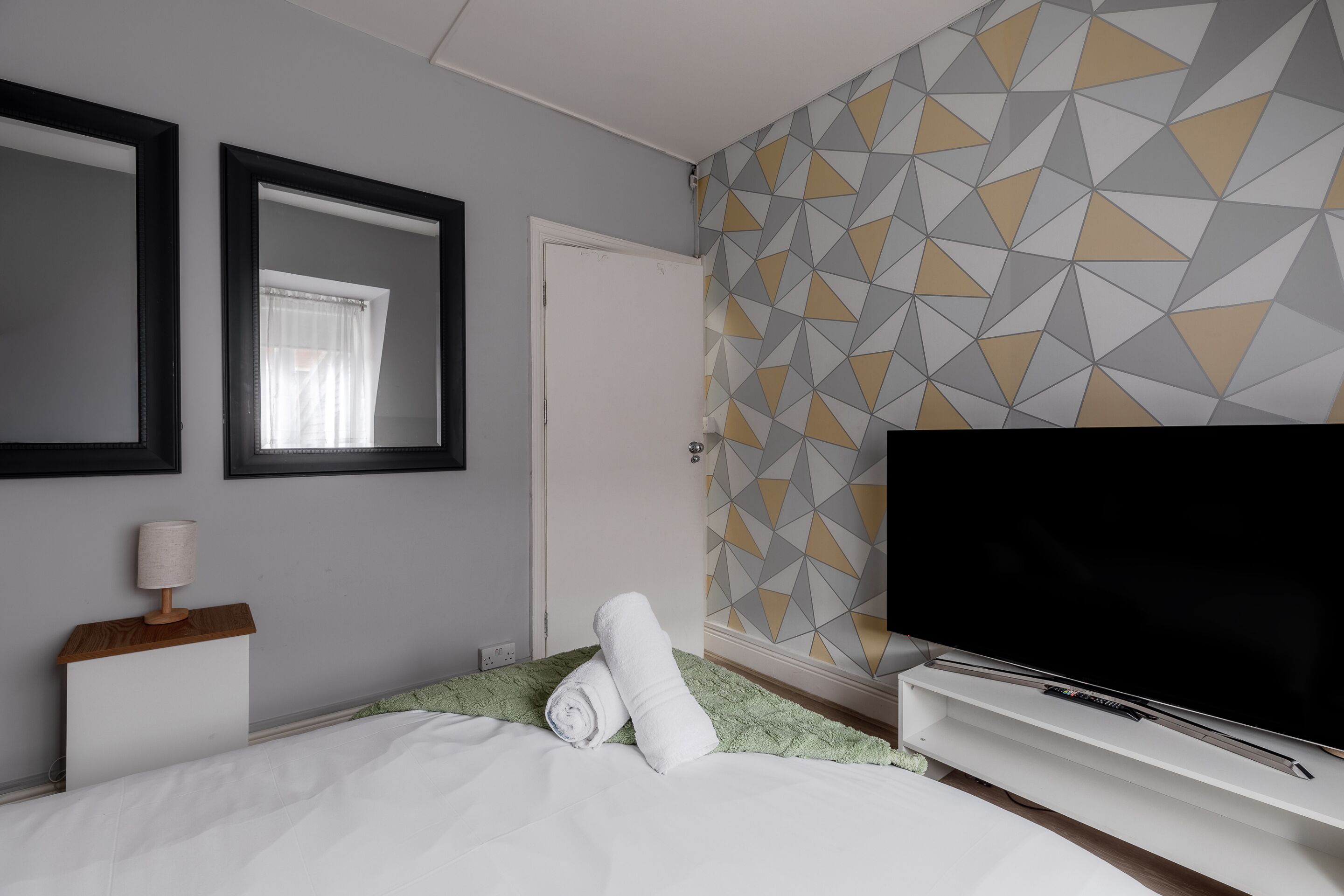 Et hotelværelse med en seng, et fjernsyn, et spejl og en væg med geometriske mønstre.