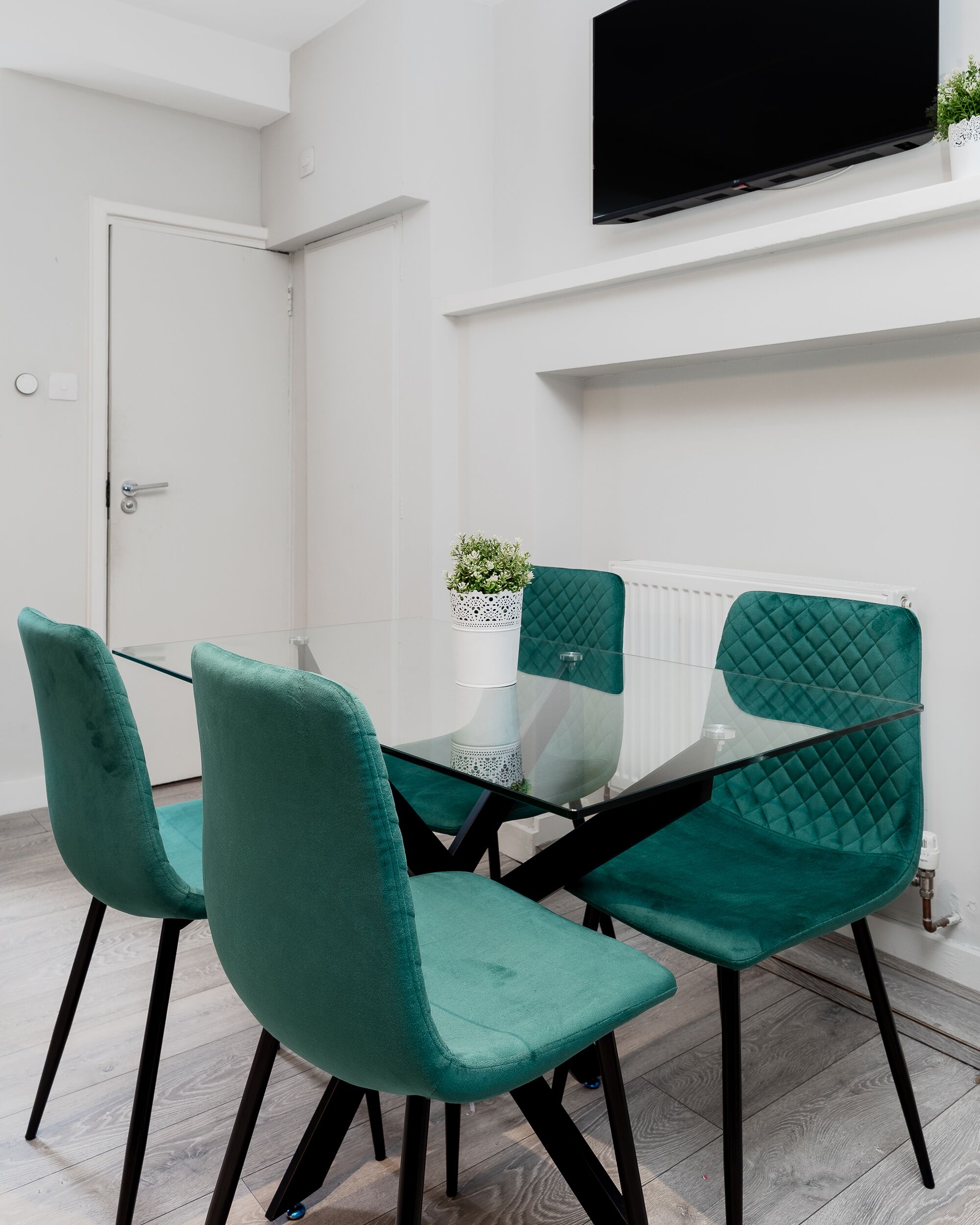 A modern room with a glass table, teal chairs, a white door, and a mounted TV.