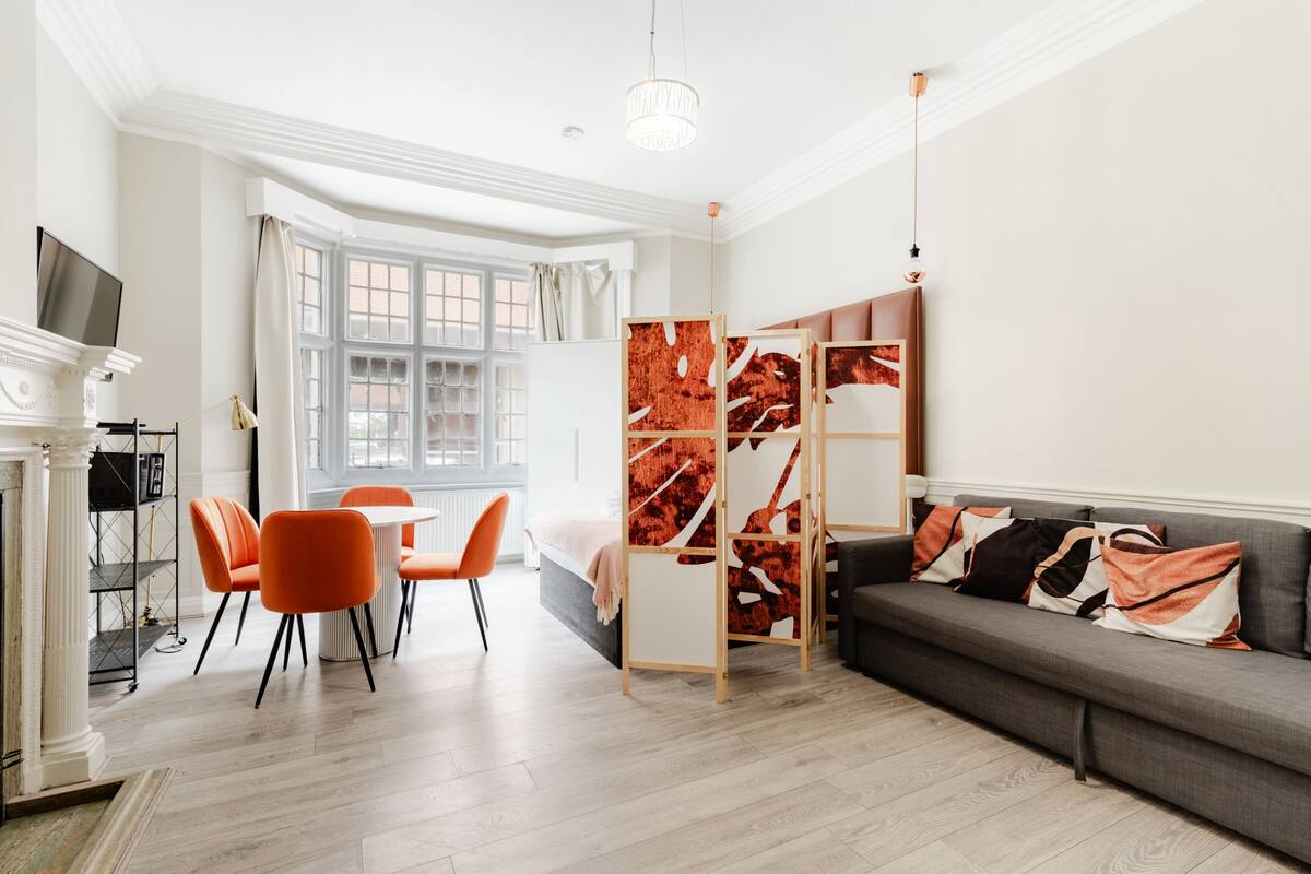 A modern living room with a sofa, orange chairs, a dining table, and a fireplace.