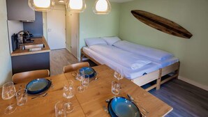 Una habitación pequeña con cama, una mesa de comedor con platos y vasos, y una tabla de surf en la pared.