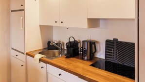 A compact kitchen with white cabinets, a wooden countertop, a sink, a kettle, and a portable grill. - Surfers Lodge | Lake View & Pool (Därligen)