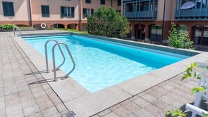 A swimming pool with metal ladders, surrounded by a tiled deck, and adjacent to a building with balconies and windows. - Surfers Lodge | Lake View & Pool (Därligen)