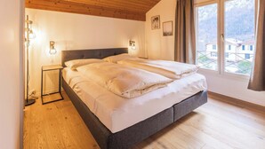 A bedroom with a large bed, wooden flooring, and a view of a mountain through a window. - Surfers Lodge | Lake View & Pool (Därligen)