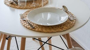 A dining table set with white plates, glasses, and cutlery on woven placemats, with chairs around it. - Surfers Studio | Lake View & Pool (Därligen)