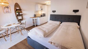 A compact hotel room with a bed, a small kitchenette, a dining area with a table and chairs, and a wall-mounted TV. - Surfers Studio | Lake View & Pool (Därligen)