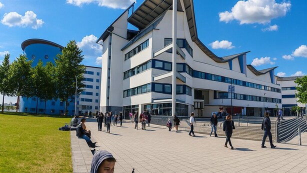 A modern building with a unique angular design, surrounded by a spacious plaza with people walking and sitting. - Room-luxury Homestay Near Excel London C (London)