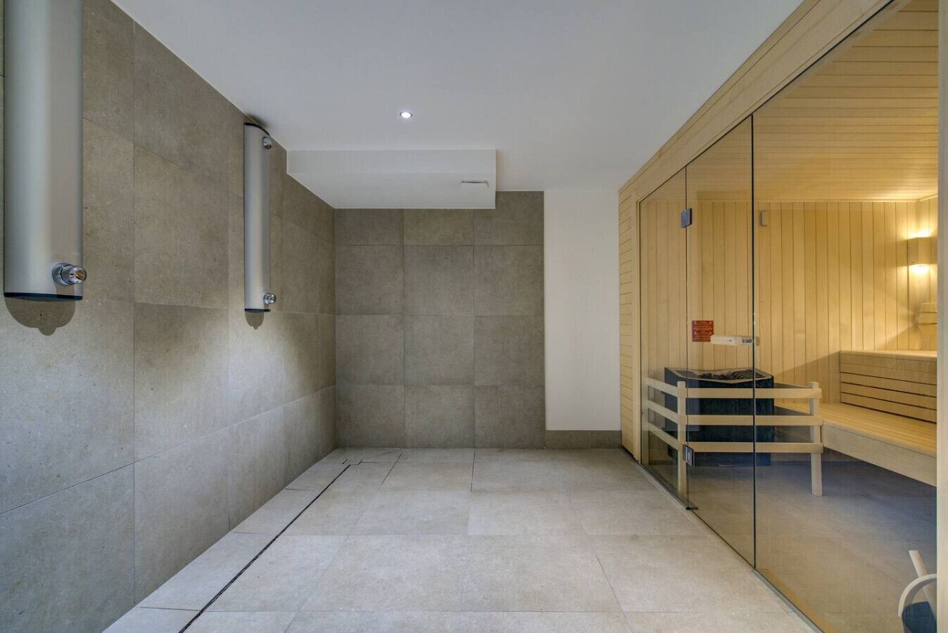 Une salle de bain moderne avec une douche à parois de verre, un sauna en bois et un sol carrelé.