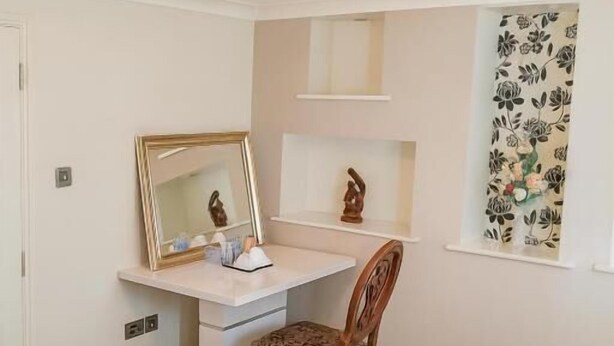 A neatly arranged bedroom with a bed, a desk, a chair, a mirror, and a window with floral curtains. - Room-luxury Room in East London Excel (London)