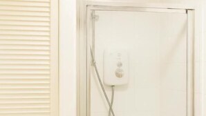 A bathroom with a glass-enclosed shower, a white tiled wall, and a door with horizontal slats. - Room-luxury Room in East London Excel (London)