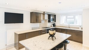 A modern kitchen with a central island, dark cabinetry, and a built-in microwave. - Room-luxury Room in East London Excel (London)