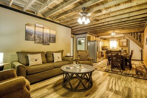 A cozy living room with a wooden ceiling, a sofa, a coffee table, and a dining area with chairs and a table. - Spirit Bear – Cabin on 4 Private Acres | Hot Tub, Game Room, Lake | Sleeps 7 (Sevierville)