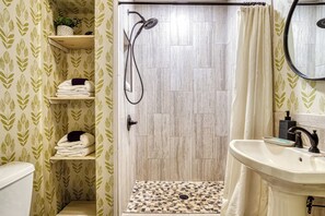 A bathroom with a shower, a sink, and shelves with towels. - Spirit Bear – Cabin on 4 Private Acres | Hot Tub, Game Room, Lake | Sleeps 7 (Sevierville)