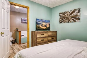 A bedroom with a bed, a dresser, a painting, and a bathroom visible through an open door. - Spirit Bear – Cabin on 4 Private Acres | Hot Tub, Game Room, Lake | Sleeps 7 (Sevierville)