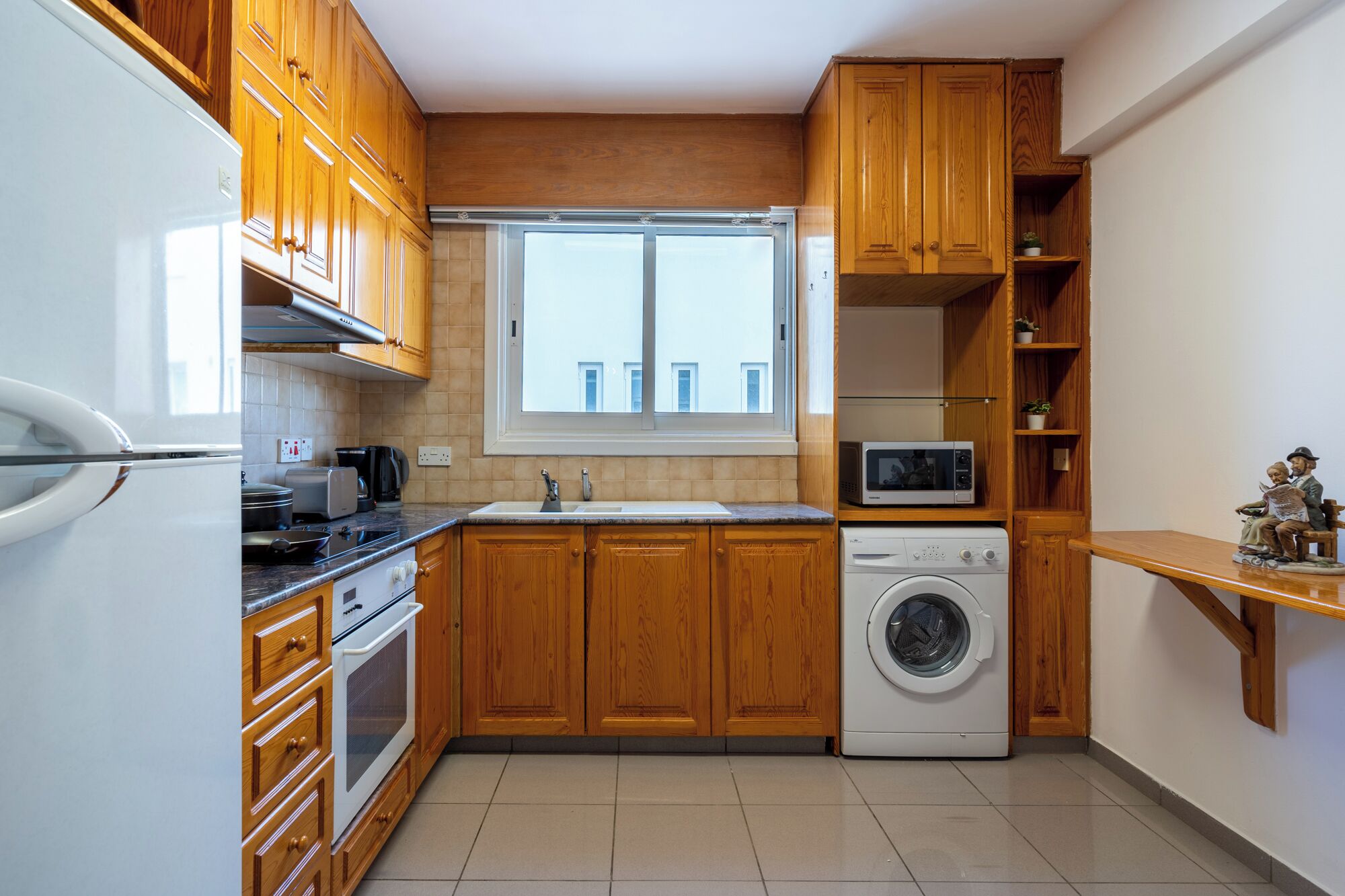 Une cuisine compacte avec des meubles en bois, un lave-linge encastré et une fenêtre qui laisse entrer la lumière naturelle.