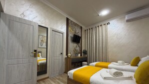 A hotel room with two beds, a wooden floor, a TV mounted on the wall, and an air conditioning unit. - Welcome Inn Hotel (Tashkent)