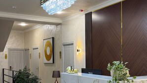 A hotel reception area with a marble counter, a chandelier, a framed artwork, and a potted plant. - Welcome Inn Hotel (Tashkent)