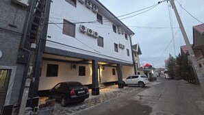 A two-story building with multiple air conditioning units, a covered parking area, and a street with parked cars. - Welcome Inn Hotel (Tashkent)
