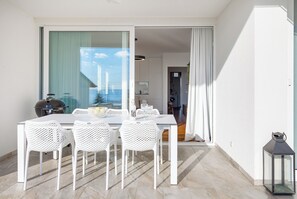 A modern dining area with a white table and chairs, a view through a glass door, and a lantern on the floor. - Apartment Lara - rooftop pool, 2 bedroom, sea view (Ičići)