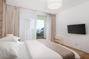 A hotel room with a bed, a TV, a window with curtains, and a view of the outdoors. - Apartment Lara - rooftop pool, 2 bedroom, sea view (Ičići)