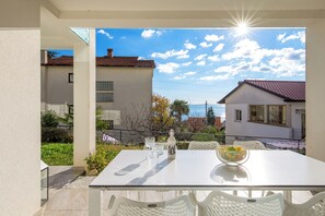 A balcony with a white table and chairs, a bottle, and a bowl of fruit. - Apartment Lara - rooftop pool, 2 bedroom, sea view (Ičići)
