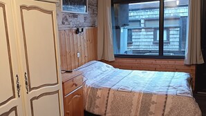 Ein Schlafzimmer mit einem Holzbett, einem Kleiderschrank, einem Fenster mit Vorhängen und einem Bild an der Wand.