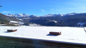Eine Dachterrasse mit freiem Blick auf schneebedeckte Berge unter blauem Himmel.