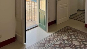 A hallway with a patterned floor, a door leading to a balcony with a view of a body of water and buildings, and an air conditioning unit on the wall. - Pietra del Bagno - Exclusive sea-view residence (Lipari)
