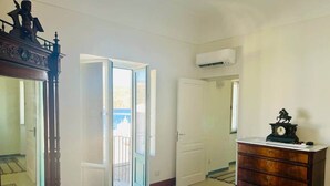 A bedroom with a bed, a dresser, a clock, and a door leading to an outdoor balcony. - Pietra del Bagno - Exclusive sea-view residence (Lipari)