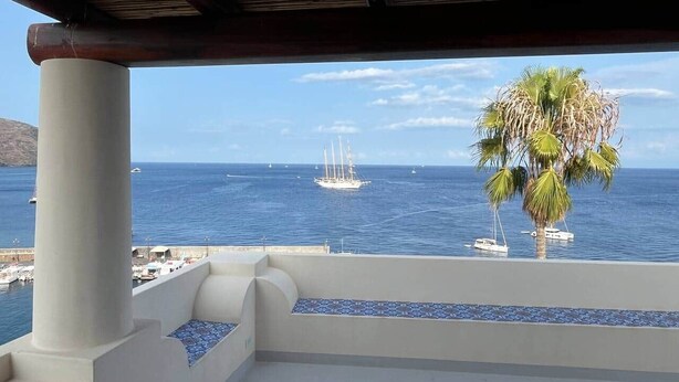 A balcony with a view of the sea, a palm tree, and a sailboat. - Pietra del Bagno - Exclusive sea-view residence (Lipari)