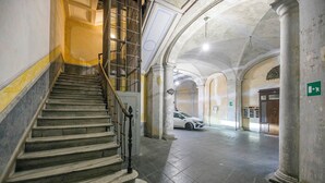 Una imponente escalera conduce a un piso superior, flanqueada por paredes y columnas de mármol, con un automóvil estacionado al fondo.