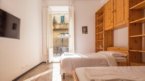 Habitación de hotel con dos camas, televisión, estanterías de madera y vistas al balcón exterior.