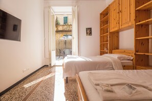 A hotel room with two beds, a TV, wooden shelves, and a view of the outside balcony. - Airy 5BR Flat with Balcony - Old Town (Genoa)