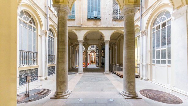 Un pasillo con columnas, ventanas en arco y un espacio abierto en el centro.