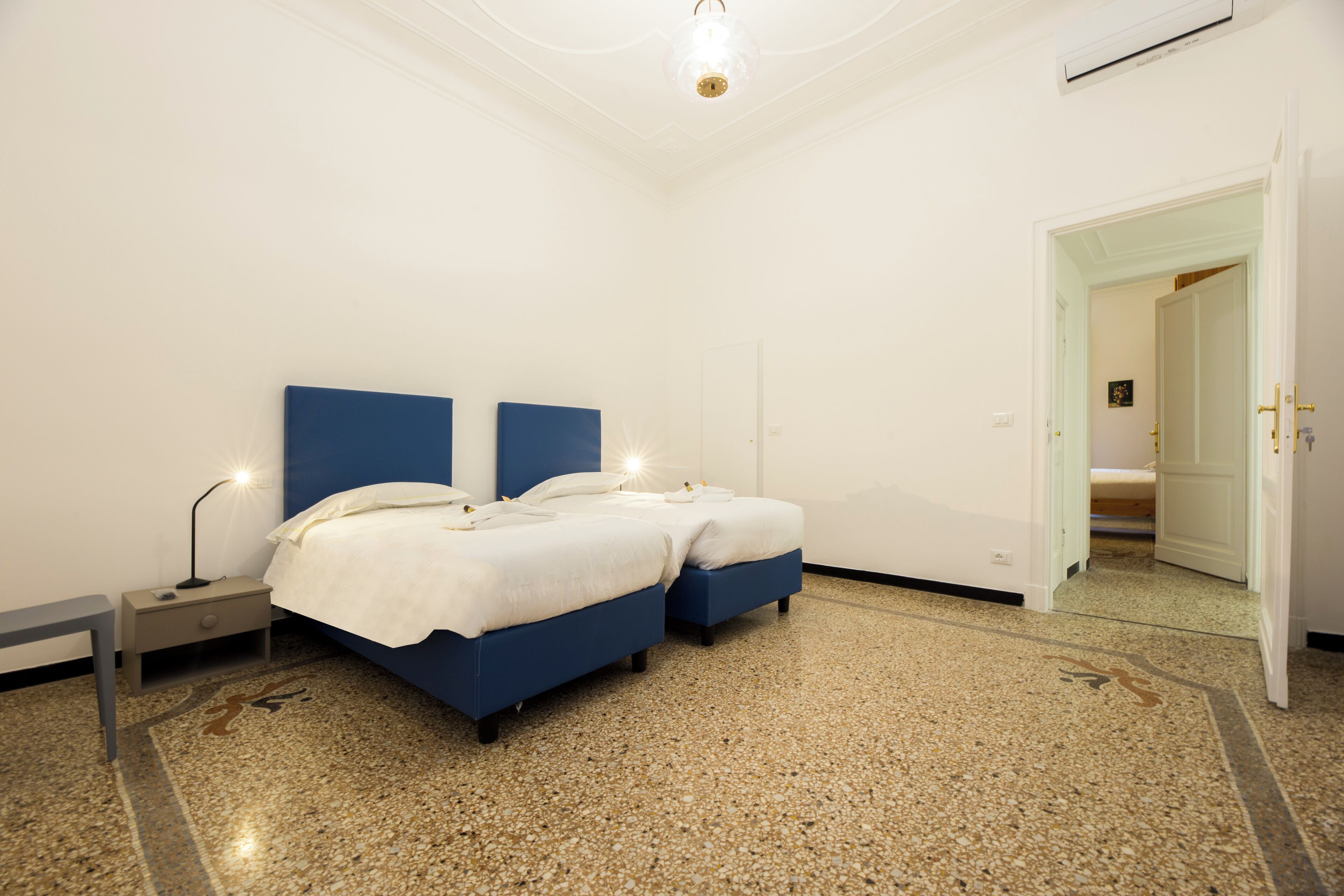 A bedroom with two beds, a nightstand, a lamp, and a door leading to another room.