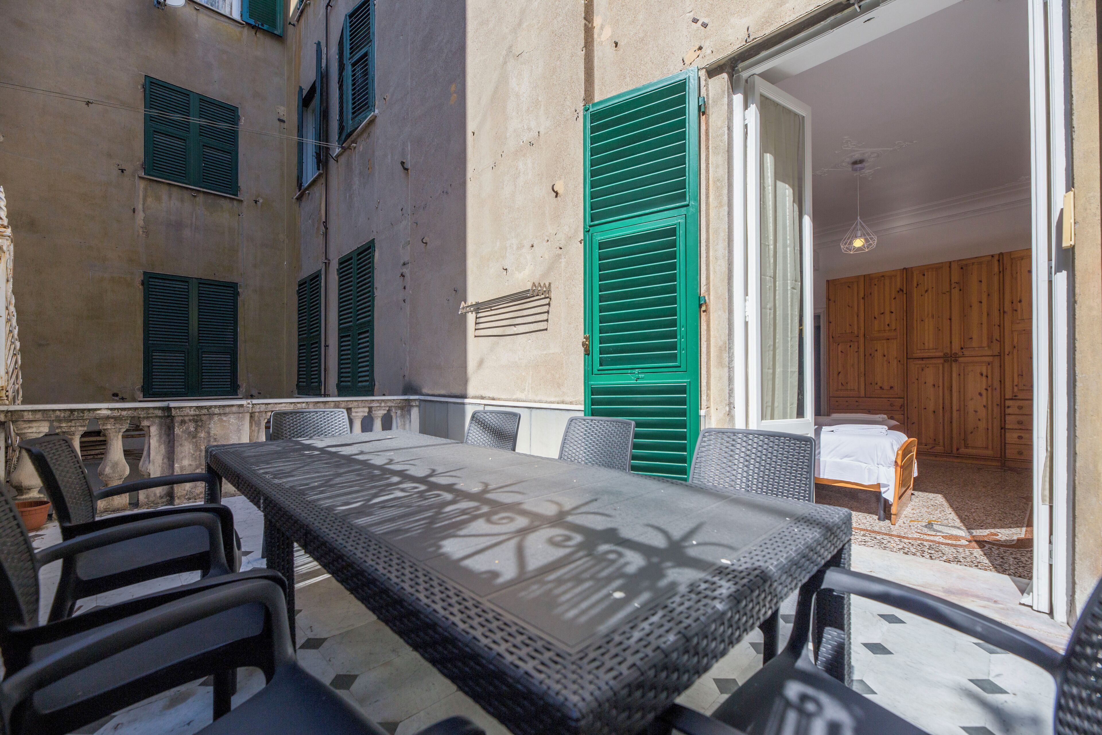 An outdoor patio with a table and chairs, a wooden door, and a bed visible inside.