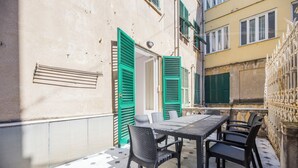 Un patio con una mesa y sillas, una puerta con contraventanas verdes y un suelo de baldosas.