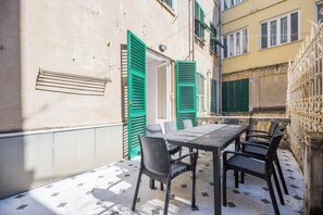 A patio with a table and chairs, a door with green shutters, and a tiled floor. - Airy 5BR Flat with Balcony - Old Town (Genoa)