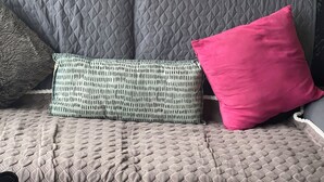 Ein graues, gepolstertes Sofa mit strukturierter Stoffbezug, zwei gemusterte Kissen und ein schlichtes rotes Kissen.