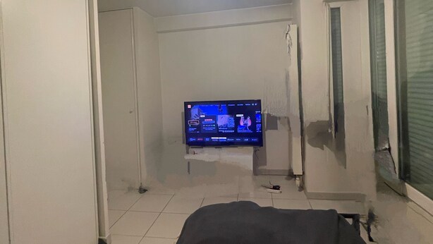 Ein Schlafzimmer mit einem Bett, einem an der Wand befestigten Fernseher und einer Deckenleuchte.