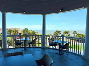 Ein überdachter Außenbereich mit Tischen und Stühlen, mit Blick auf Strand und Meer.