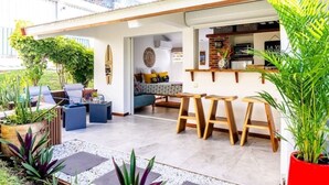 An outdoor patio area with seating, a kitchen visible through an open door, and potted plants. - La Rose Bleue - Your renovated cocoon a stone's throw from Le Diamant beach (Le Diamant)