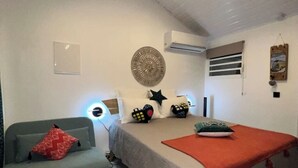 A bedroom with a bed, a sofa, an air conditioner, and a wall-mounted decorative item. - La Rose Bleue - Your renovated cocoon a stone's throw from Le Diamant beach (Le Diamant)