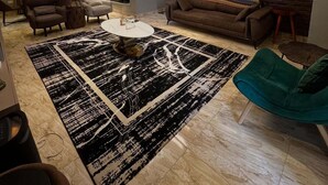 Ein modernes Wohnzimmer mit einem großen Teppich in Schwarz-Weiß-Muster, einem braunen Sofa, einem türkisfarbenen Sessel und einem Couchtisch.