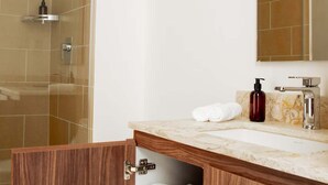 Ein Badezimmer mit Dusche, einem Waschbecken mit Marmorplatte, einem Holzschrank mit Handtüchern und einem Spiegel über dem Waschbecken.