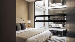 Ein modernes Hotelzimmer mit einem großen Bett, einem Fenster mit Blick auf die Stadt und einem kleinen Nachttisch mit Lampe.
