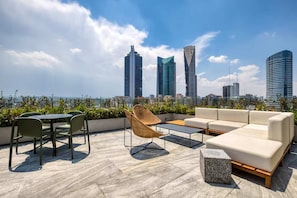 Eine Dachterrasse mit Essbereich und Lounge-Bereich, mit Blick auf eine Stadtlandschaft und moderne Gebäude.