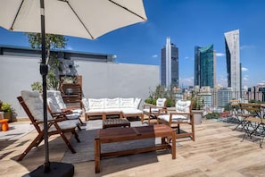 Eine Dachterrasse mit Gartenmöbeln, darunter Sofas und Stühle, und Blick auf eine Stadtlandschaft mit modernen Gebäuden.